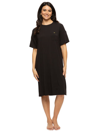 Woman wearing black sleepwear stands and smiles.